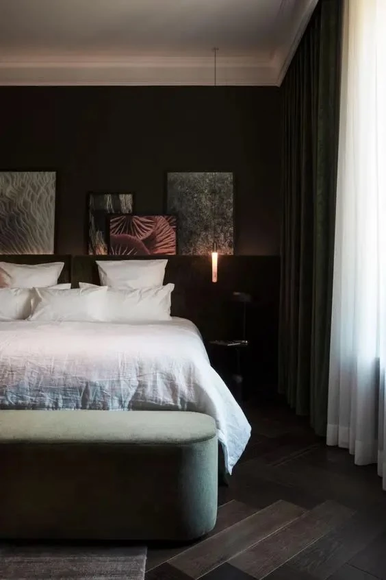 a-sophisticated-dark-bedroom-with-a-ledge-with-artwork-a-bed-with-white-bedding-a-green-curved-bench-pendant-lamps