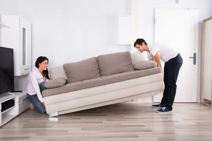 A man and woman trying to lift sofa