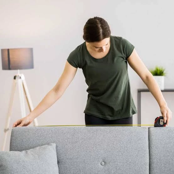 A woman measuring the width of a sofa